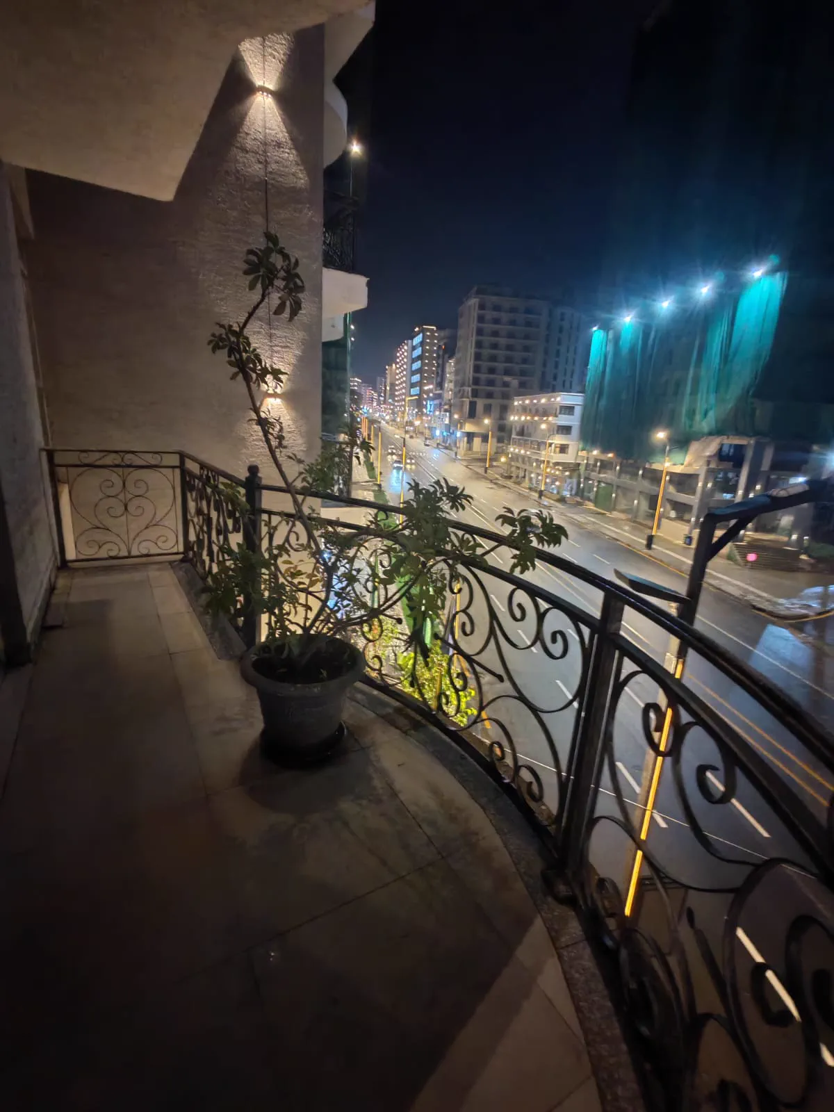 View from a wrought-iron hotel balcony over a wet Addis Ababa street lit up at night