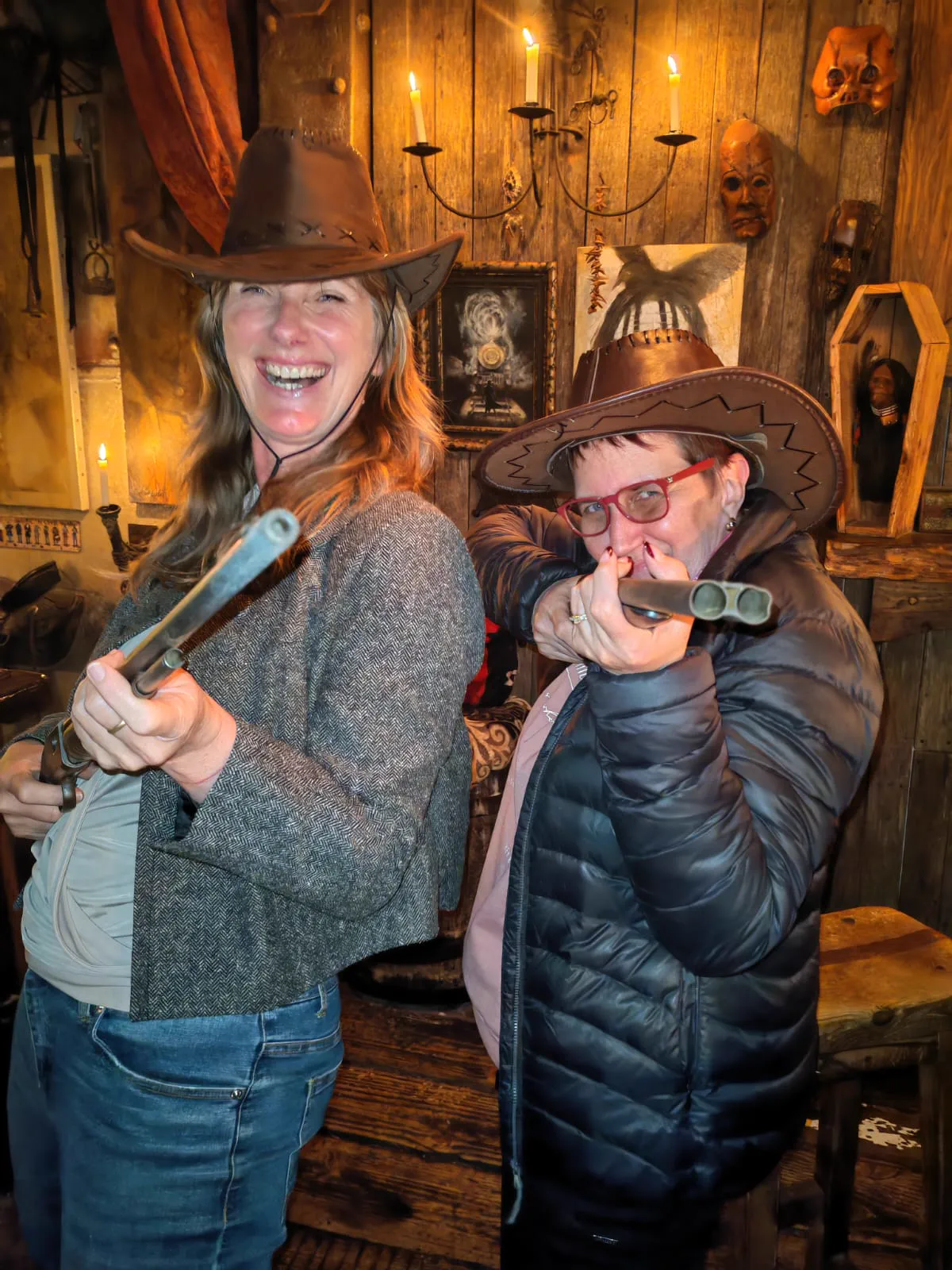 Two women in cowboy hats larking about with prop rifles at the Dust and Dynamite cowboy bar in Cape Town