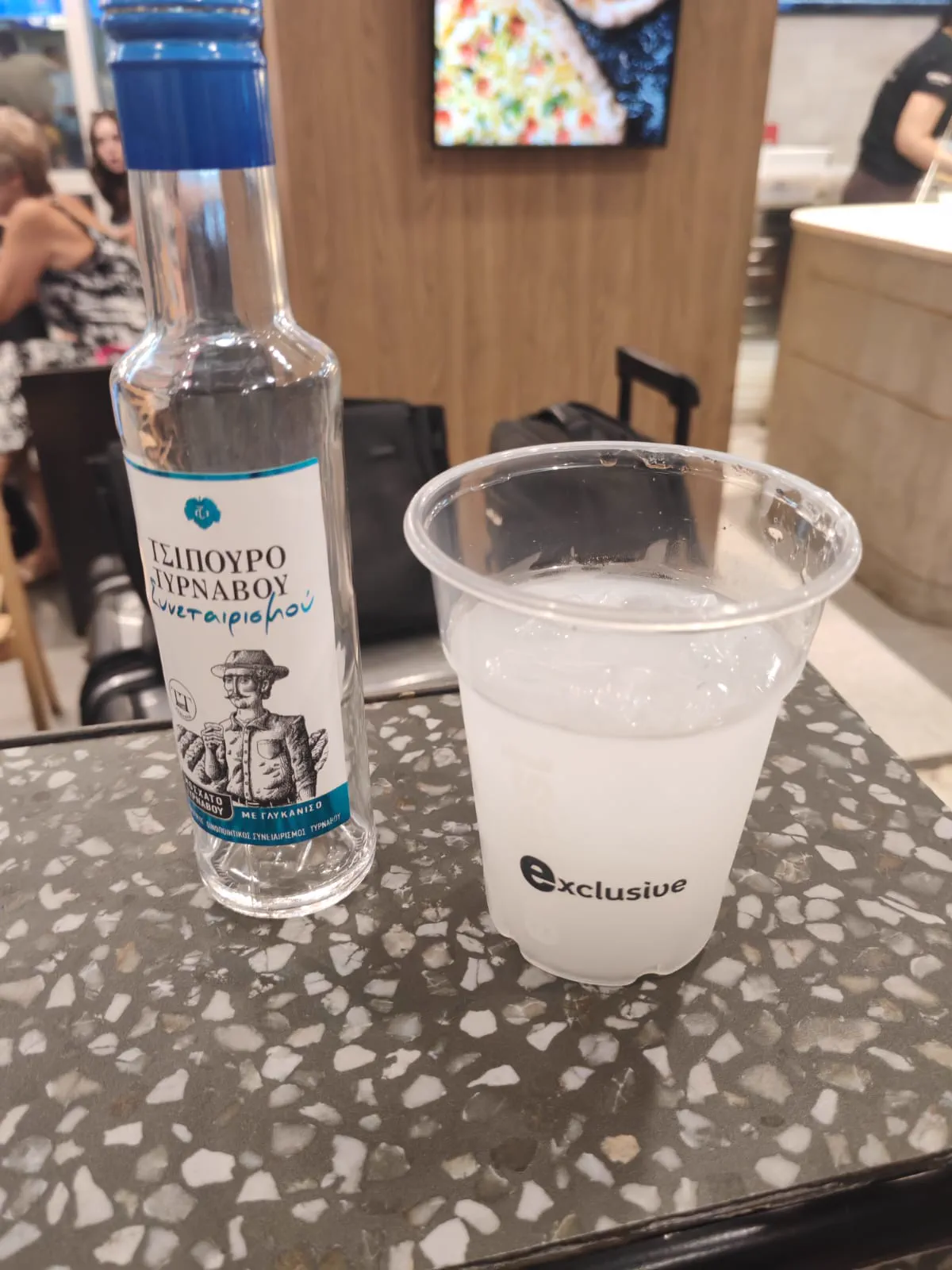 A bottle of Greek tsipouro anise spirit beside a cloudy iced glass, an arrival drink at Athens airport