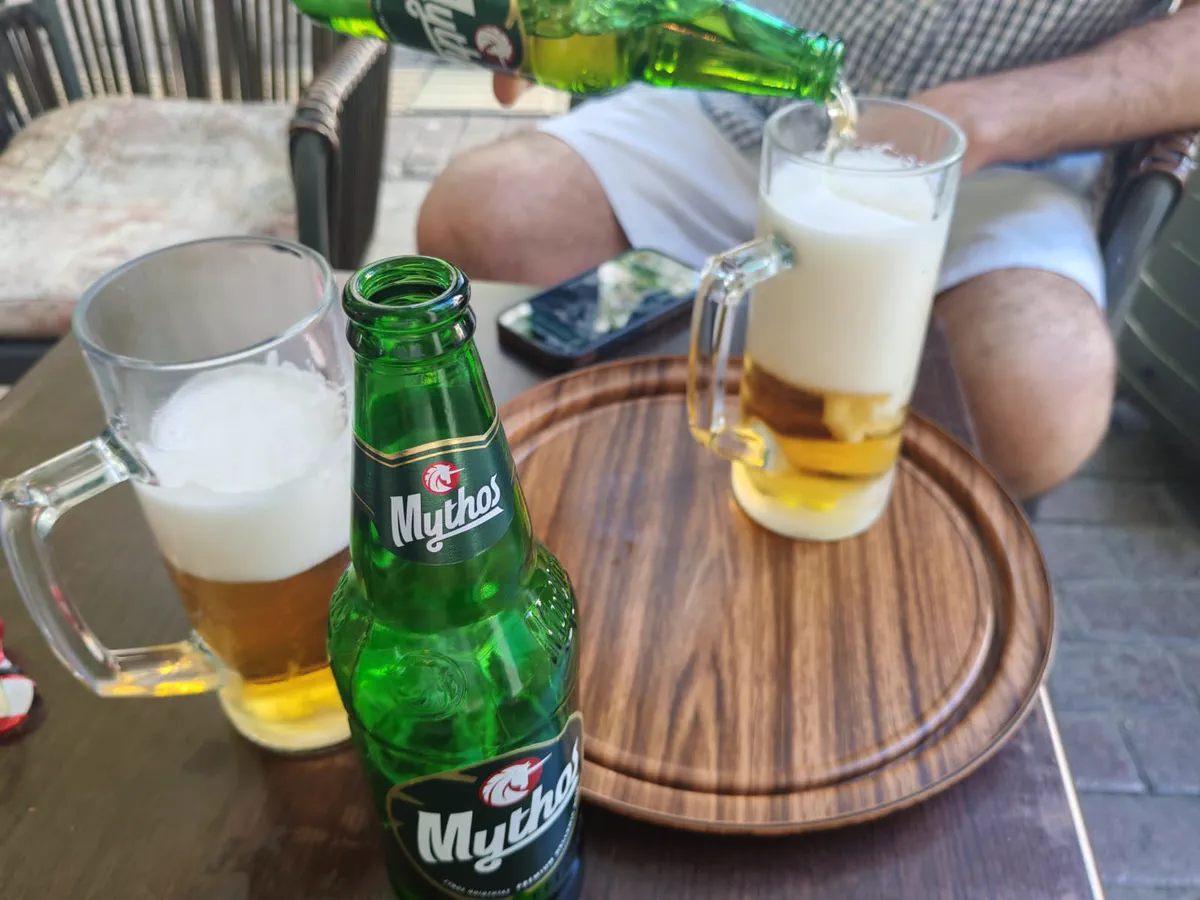 A bottle of Mythos beer being poured into a glass at an outdoor table in Athens