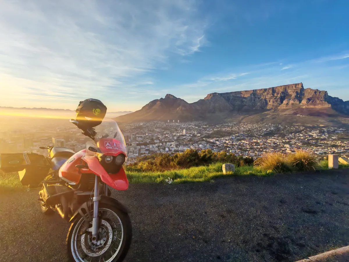 A motorbike at a viewpoint at sunrise with Table Mountain and the city of Cape Town spread out below