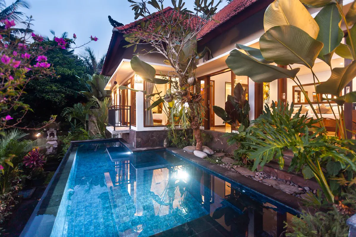 Balinese villa with a lit pool and tropical garden at dusk