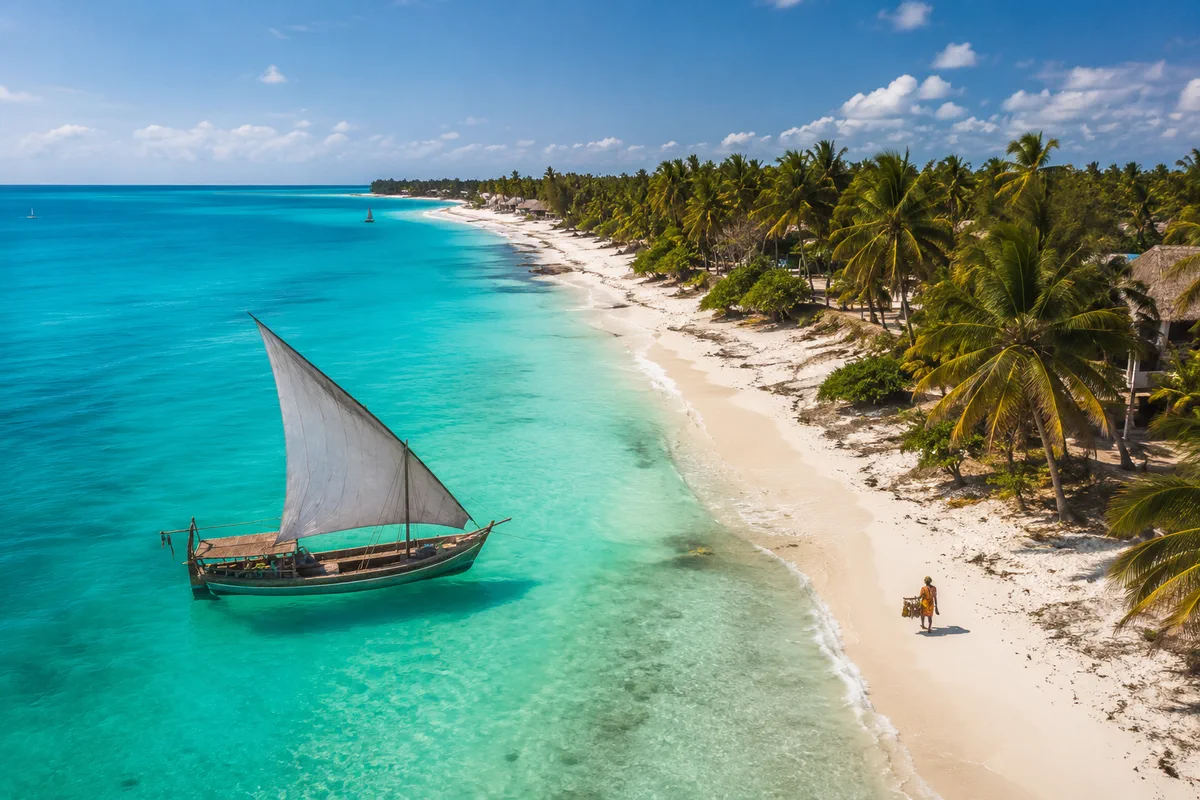 Aerial view of a turquoise Kenyan lagoon meeting a palm-fringed white-sand beach with a traditional dhow