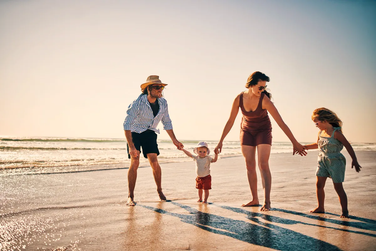 Family holding hands as they walk along the water's edge at sunset