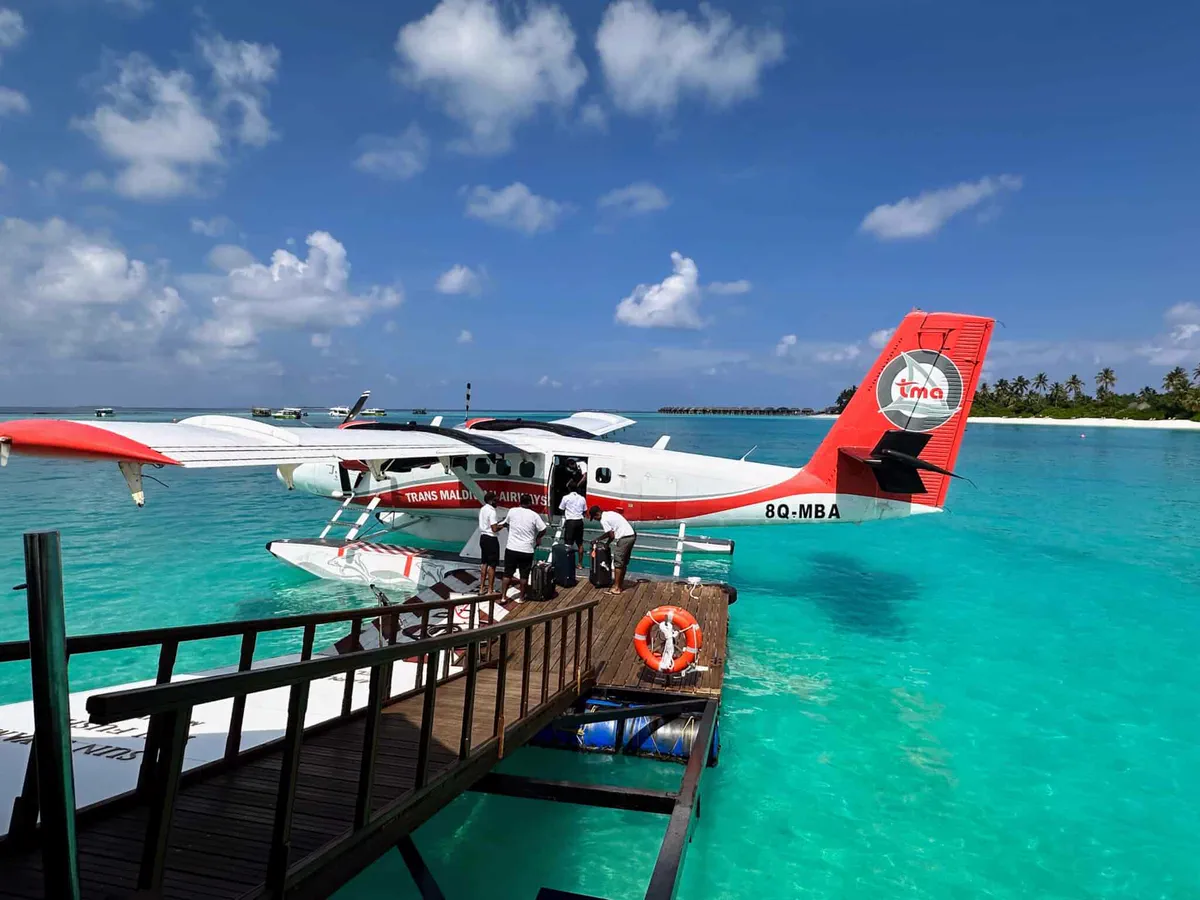 Seaplane moored at a floating jetty on a turquoise Maldives lagoon as luggage is unloaded