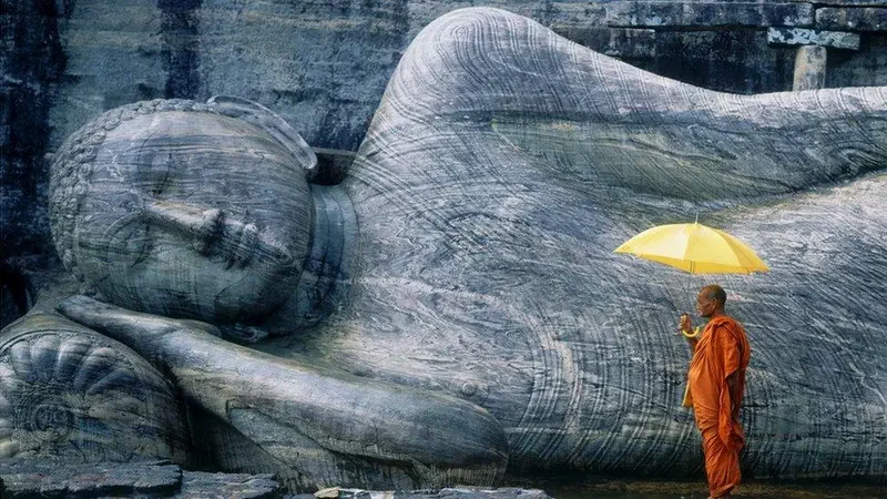 Buddhist monk with a yellow umbrella beside the reclining Buddha of Gal Vihara, Polonnaruwa, Sri Lanka