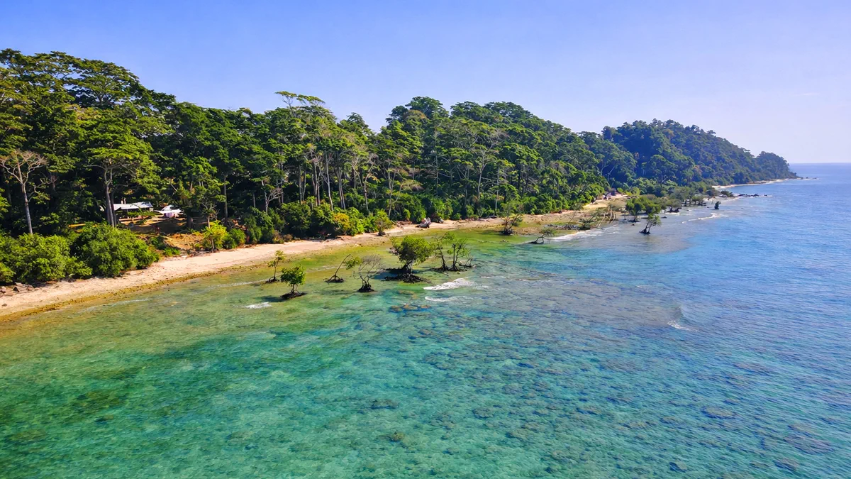 Forested coastline and a sandy beach above clear, shallow reef in the Andaman Sea
