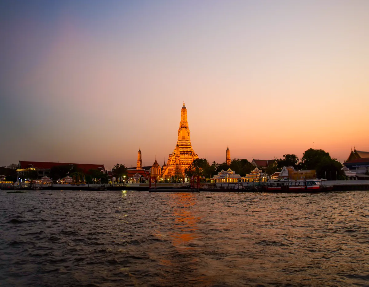 Wat Arun lit up at dusk across the Chao Phraya River, Bangkok