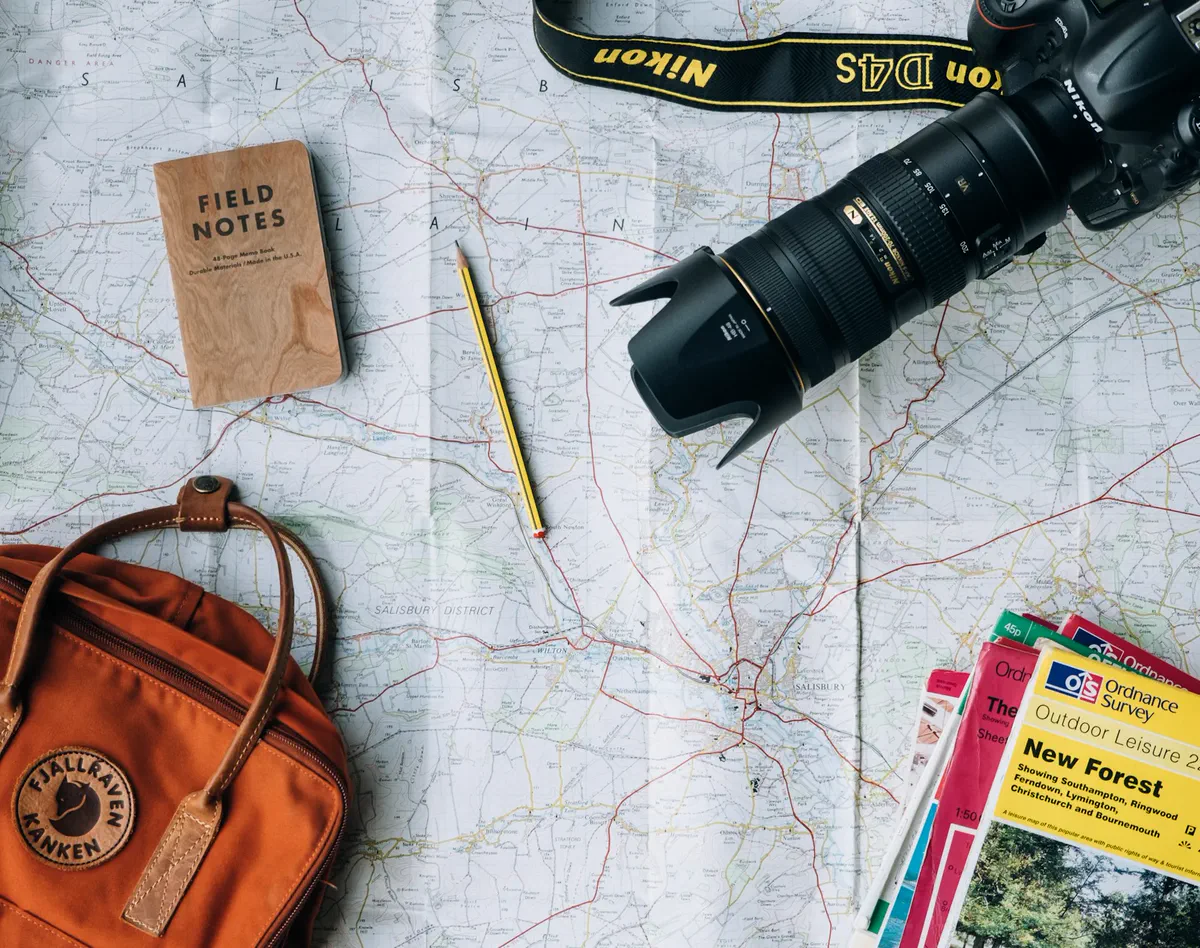 Travel planning flat lay with a map, notebook, pencil, camera and backpack