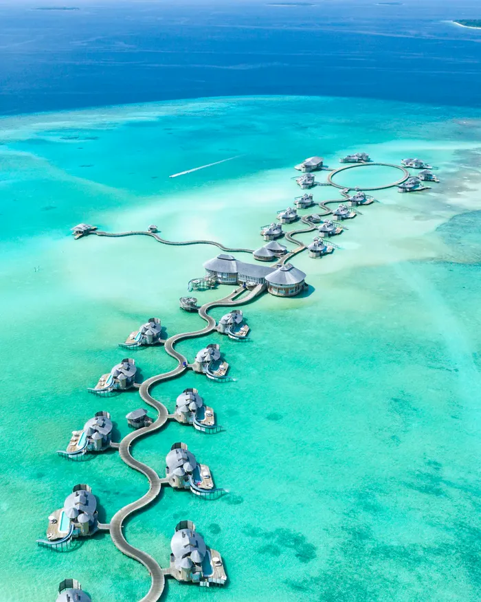Aerial view of overwater villas joined by a winding boardwalk over a turquoise Maldives lagoon